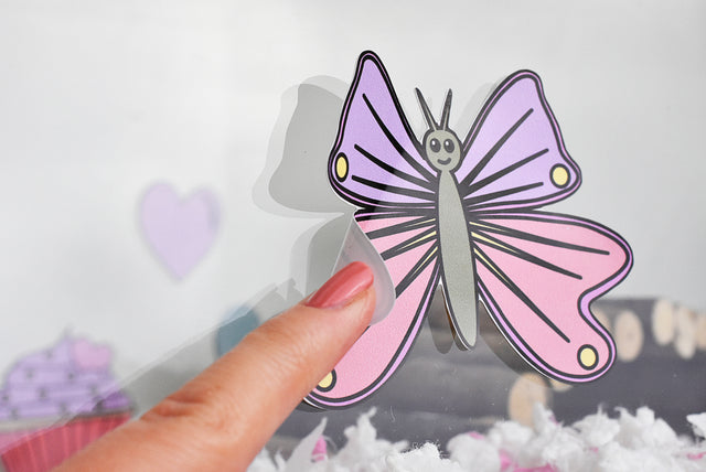 A finger turning up the corner of a Furnishables butterfly static cling sticker attached to a glass hamster habitat. 