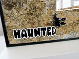 A Furnishables static cling name sticker in a spooky style font with a witch decal, stuck to the front of a glass pet enclosure.