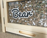 A Furnishables name sticker that says "Bear" on the front of a small pet habitat